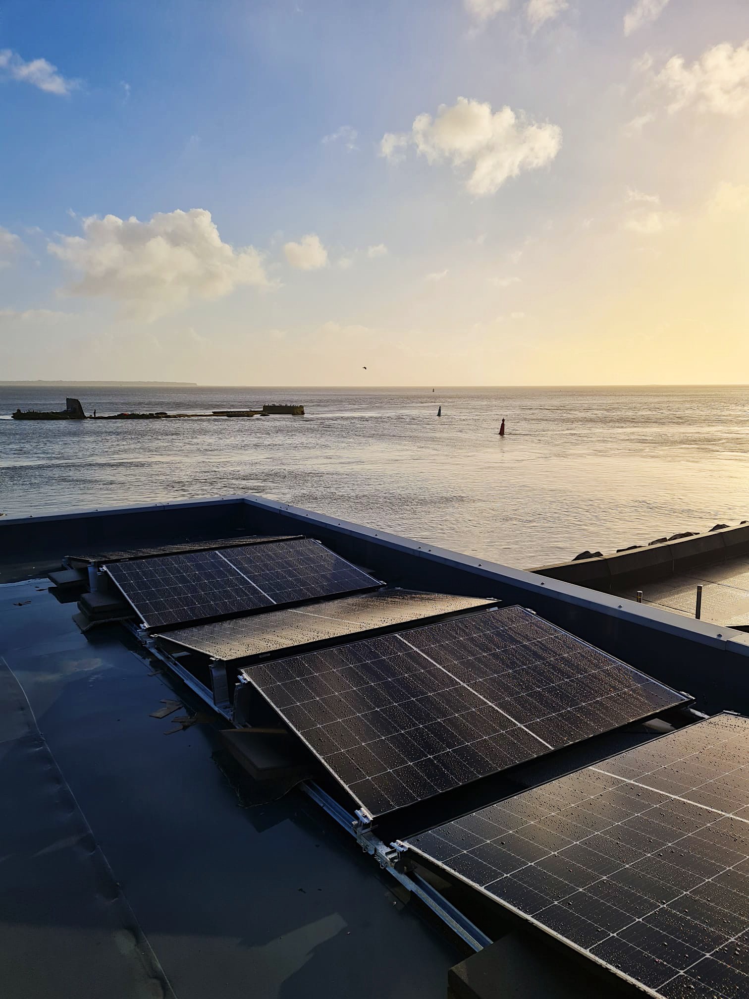 Three sets of PV solar panels on a roof, with the sea in the background at sunset.